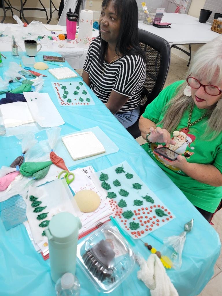 Two women working on a craft project at a table covered with supplies and decorations