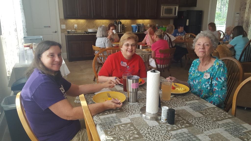 Three women smiling at the dining table during breakfast with other guests in the background